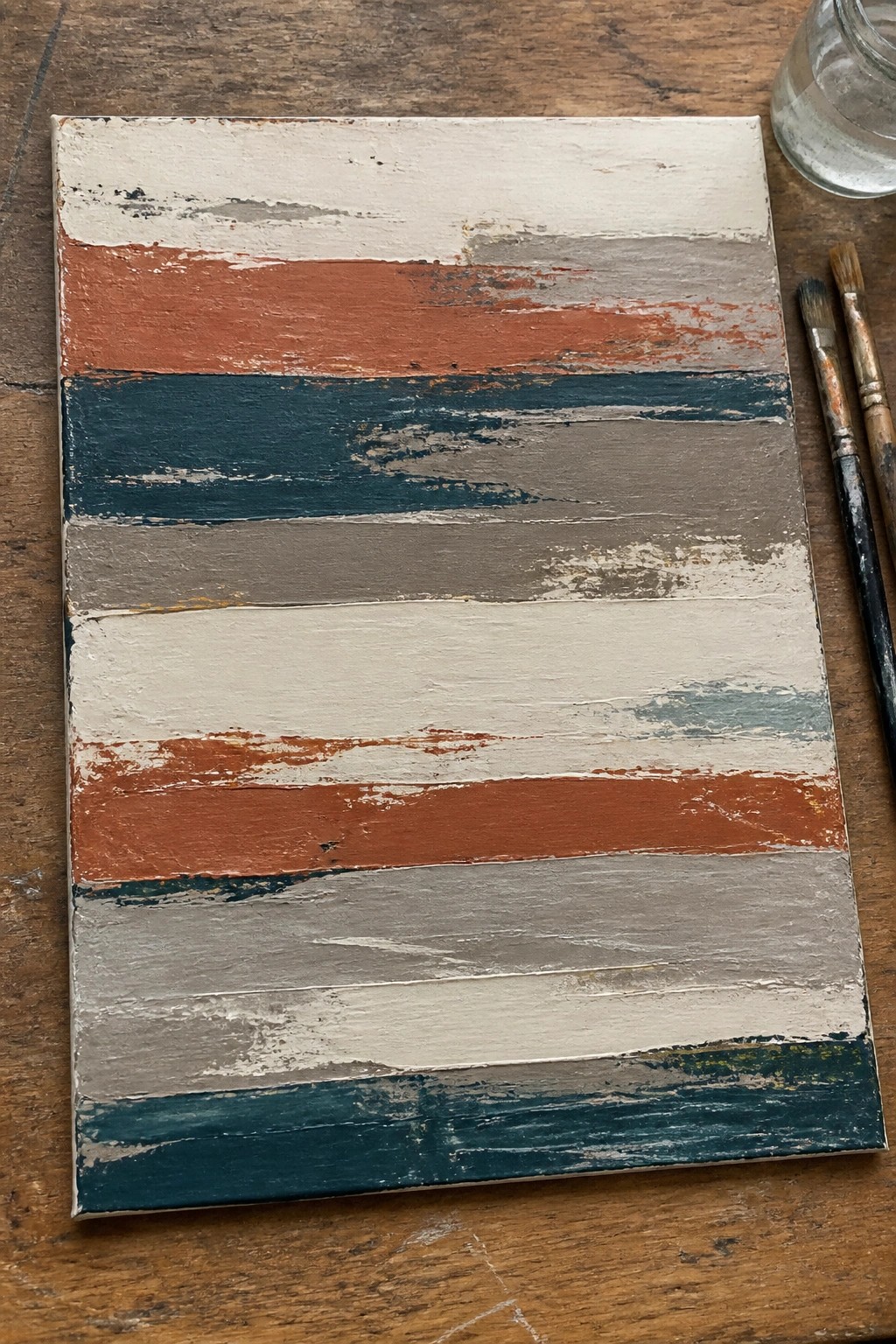 Abstract canvas with horizontal stripes in white, orange, teal, and gray beside paintbrushes