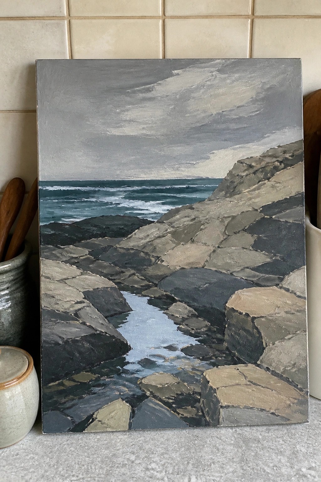 Rocky coastline painting with tidal stream, jagged rocks, and teal waves under gray sky