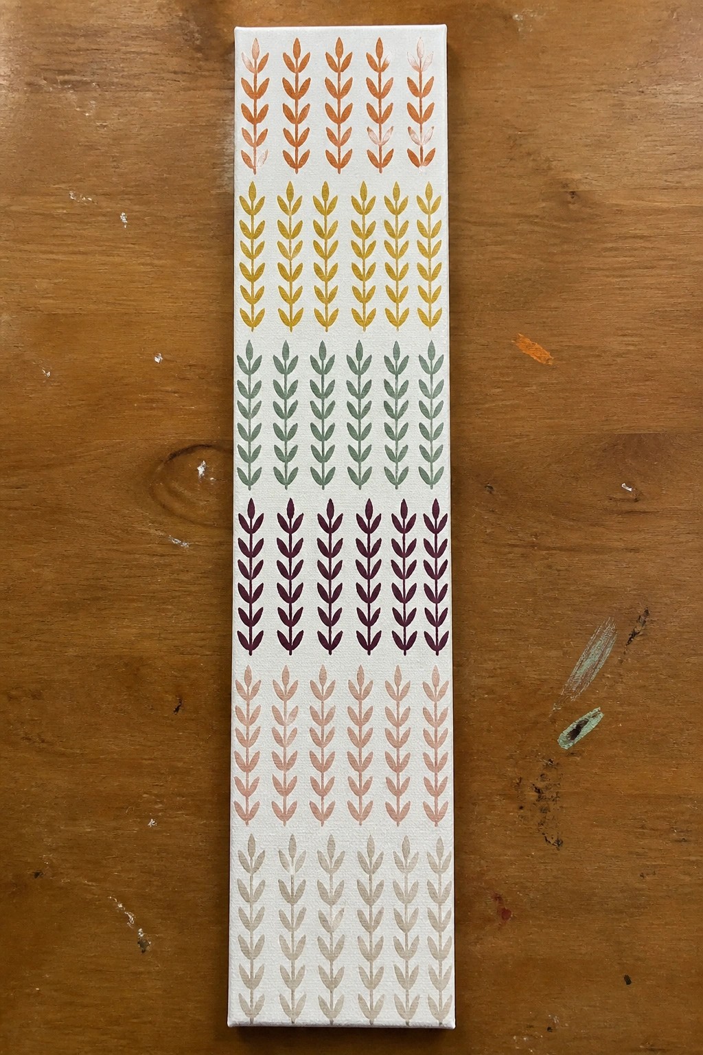 Tall canvas with horizontal rows of colorful stylized leaf patterns on wood table