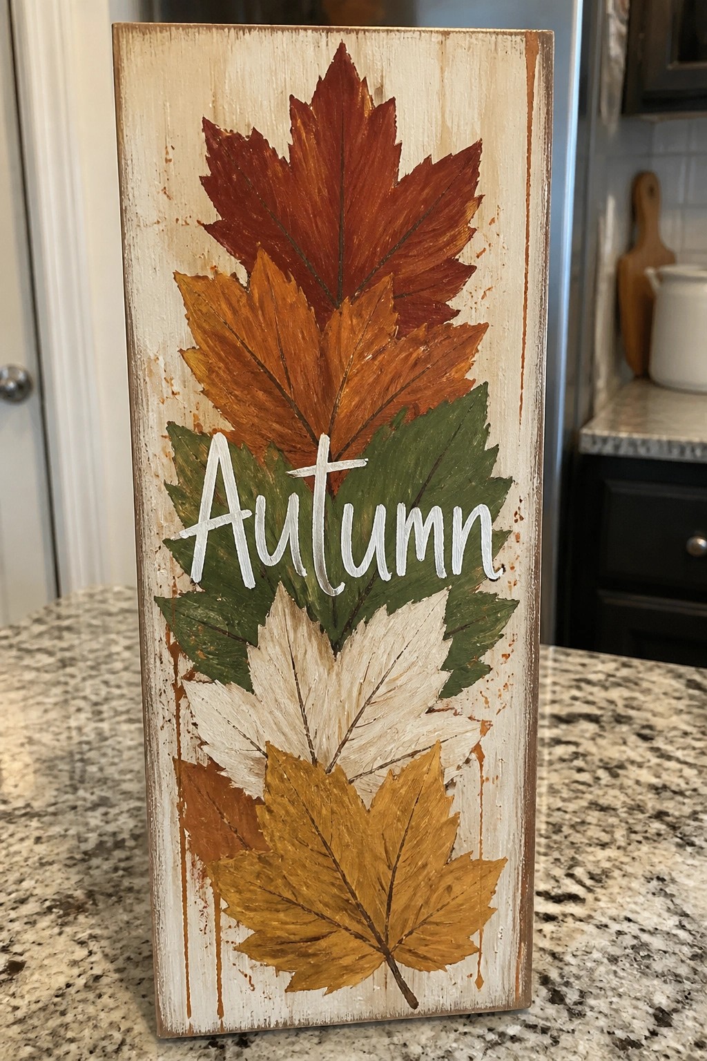 Distressed wooden sign with stacked fall leaves in red, orange, green, and yellow, labeled Autumn