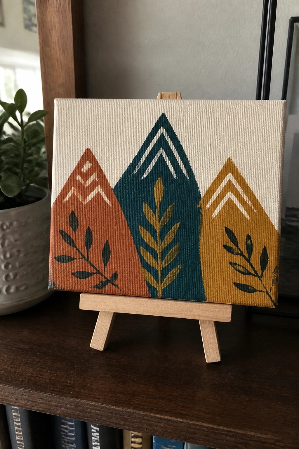 Abstract canvas on wooden easel with three geometric peaks in orange, teal, and gold