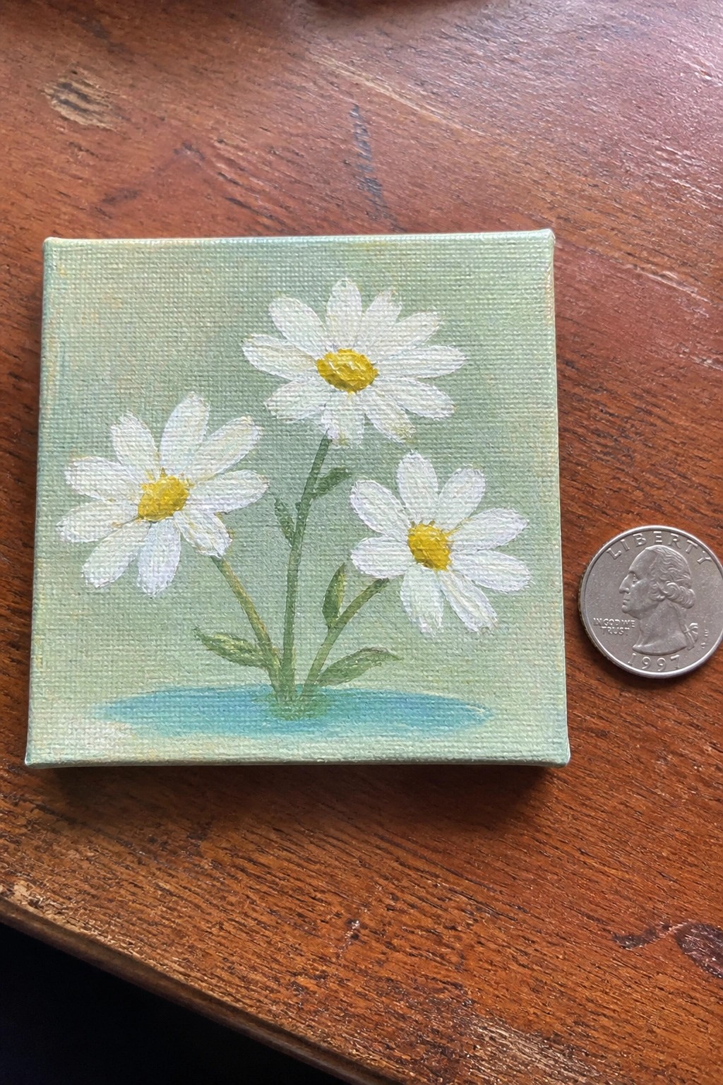 Small canvas of three white daisies with yellow centers beside a quarter