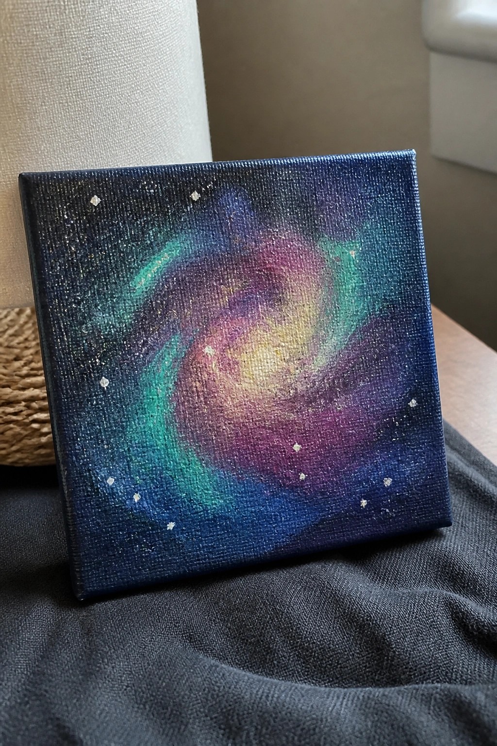 Swirling galaxy painting on square canvas with colorful nebulae and scattered stars on dark fabric