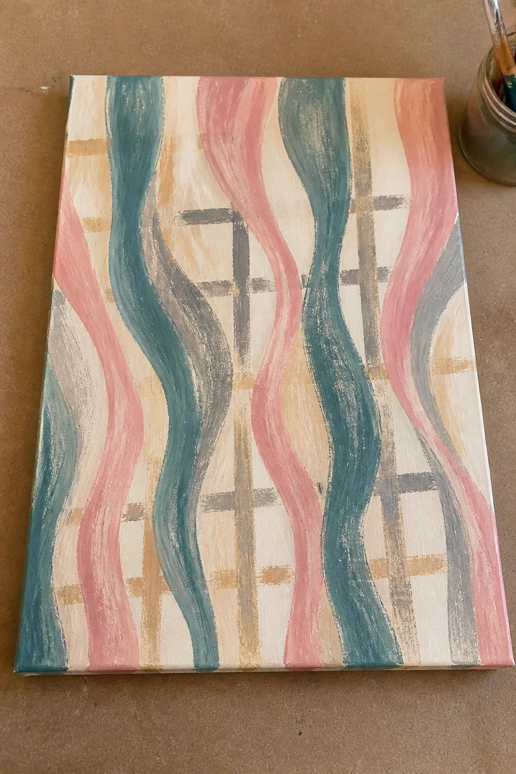 Wavy abstract canvas painting in pink, teal, and gray over grid pattern beside paint jar.