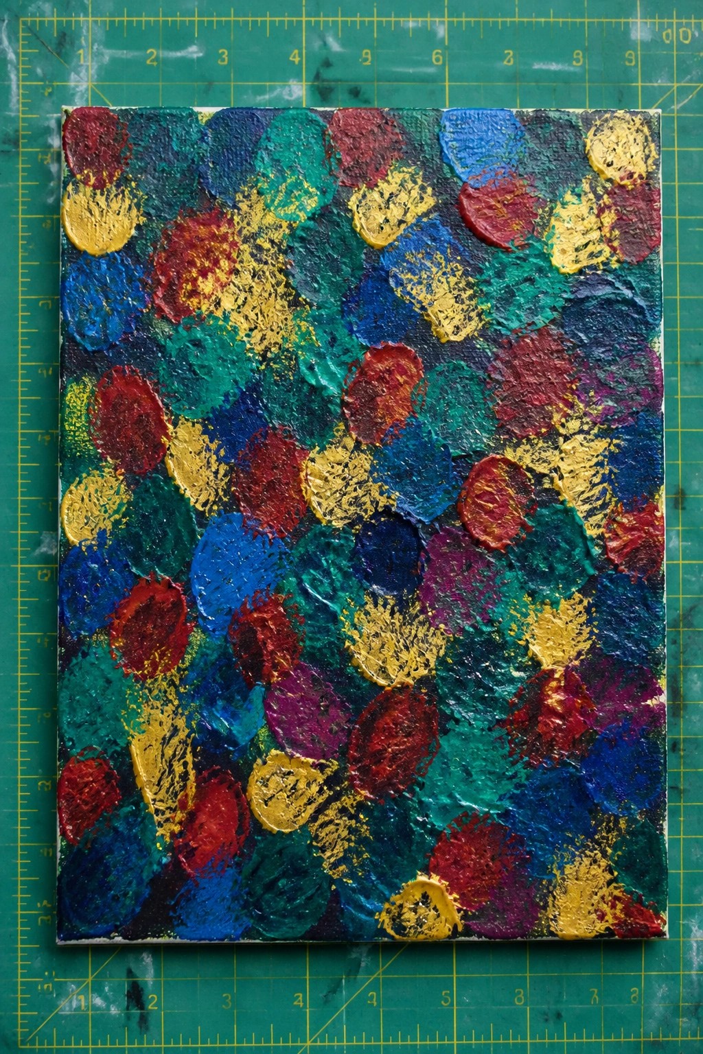 Abstract painting with thick colorful textured shapes on green cutting mat