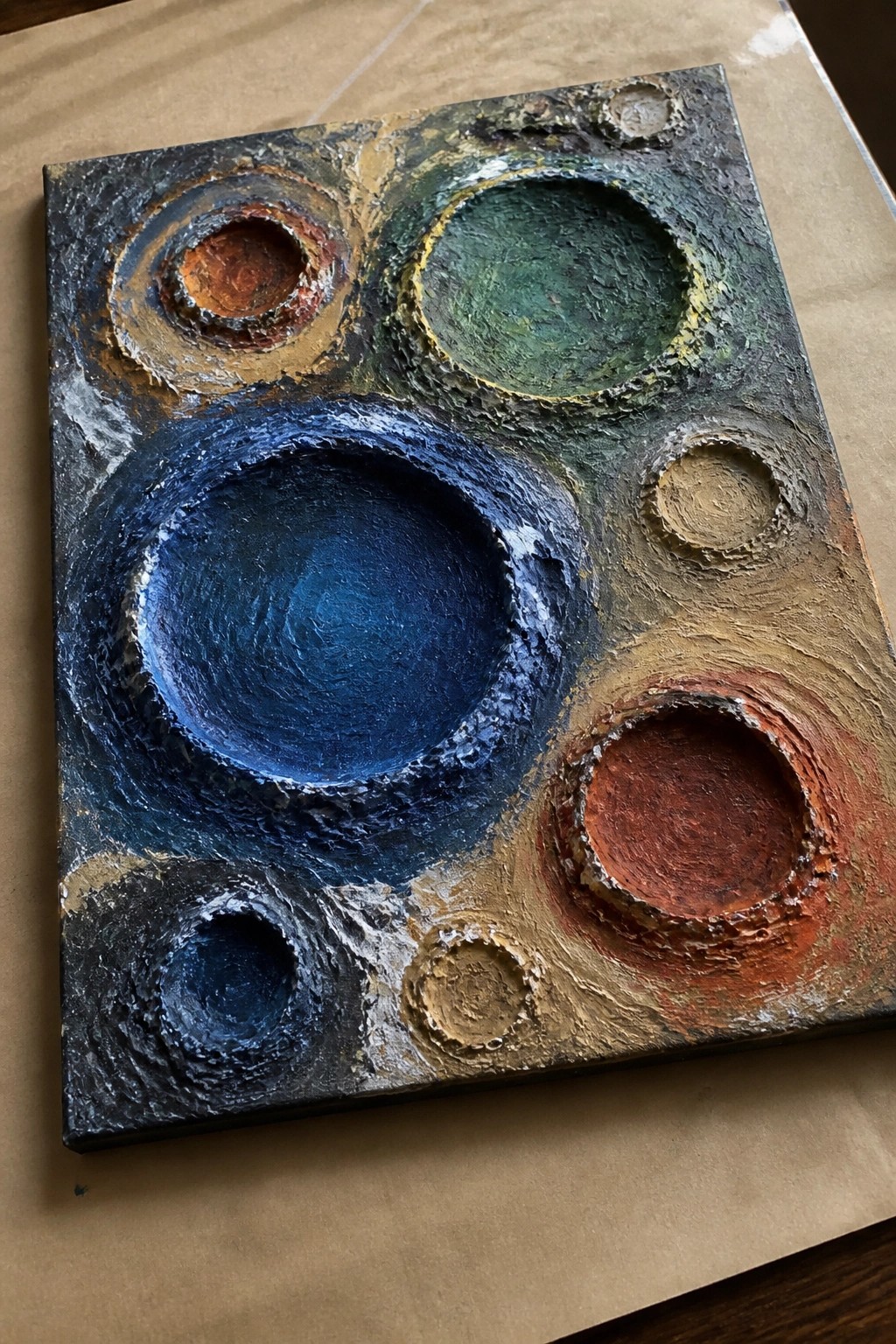 An abstract acrylic painting with several heavily textured circles in shades of blue, green, red, and earth tones.