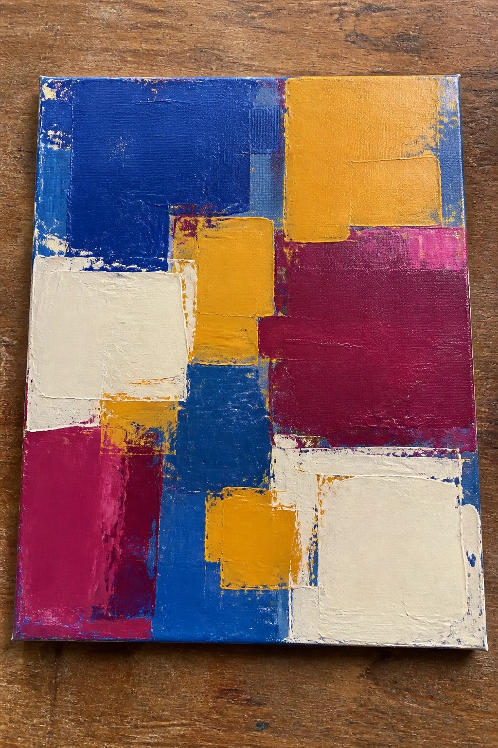 Abstract painting with blue, yellow, magenta, red, and white geometric blocks on wood