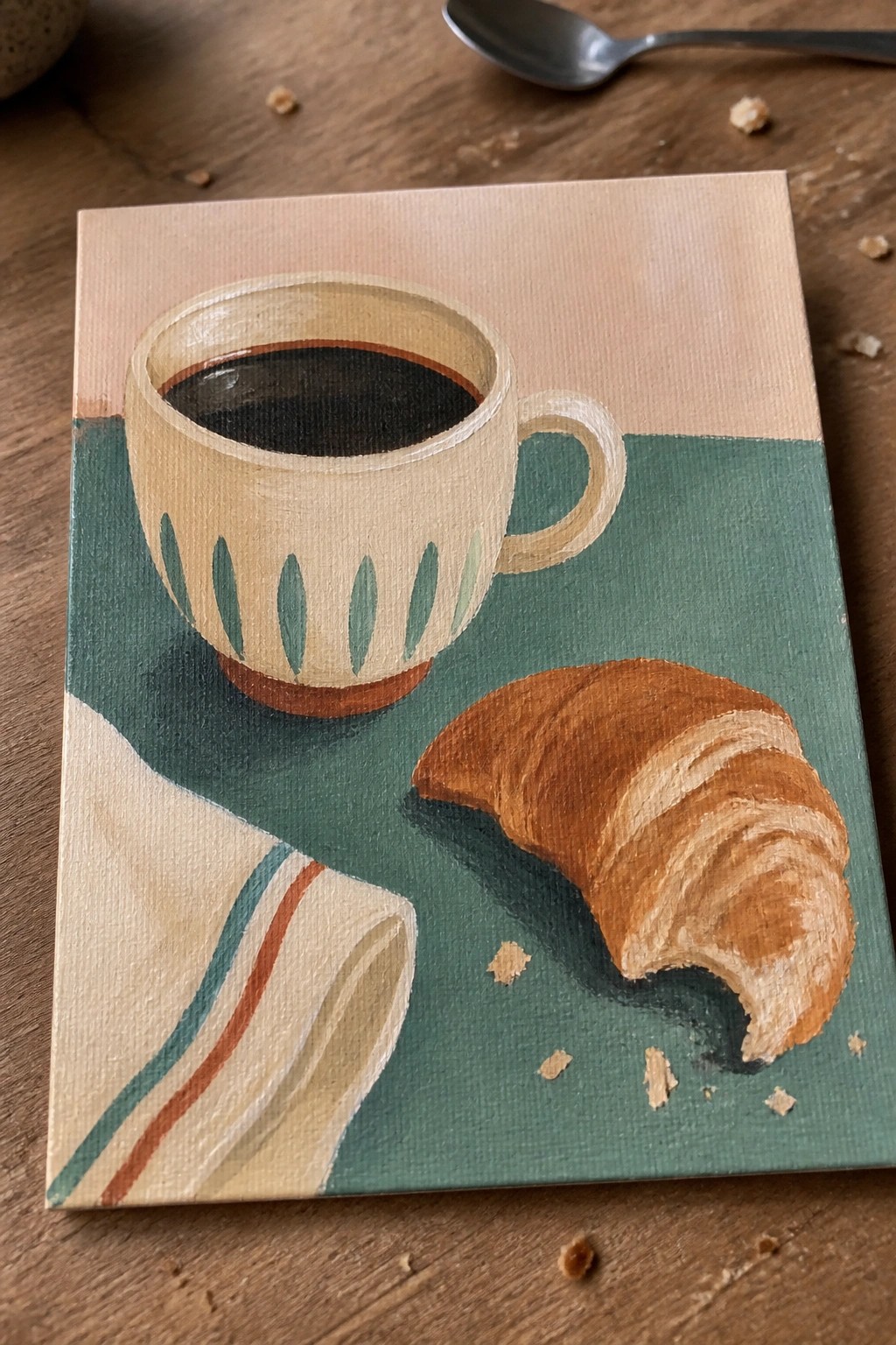 Coffee cup, croissant, and striped napkin on green surface with crumbs.
