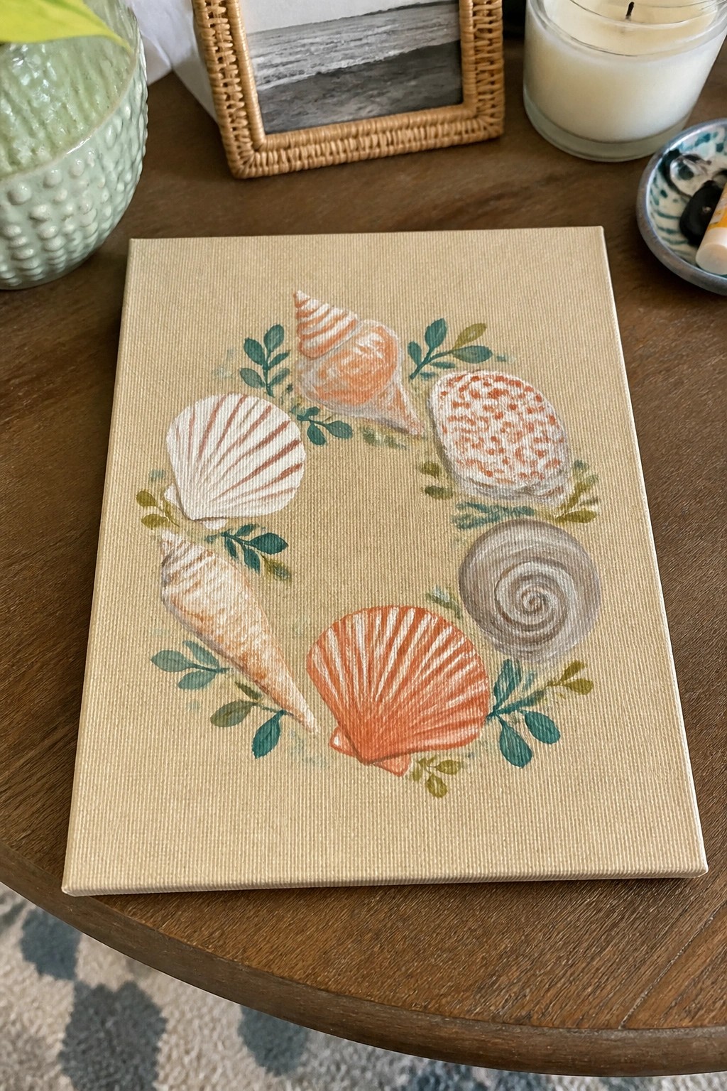 Canvas painting of colorful seashells in leafy wreath on wooden table