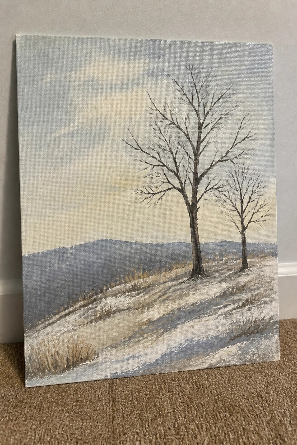 Landscape painting of two bare trees on snowy hill with distant mountains.
