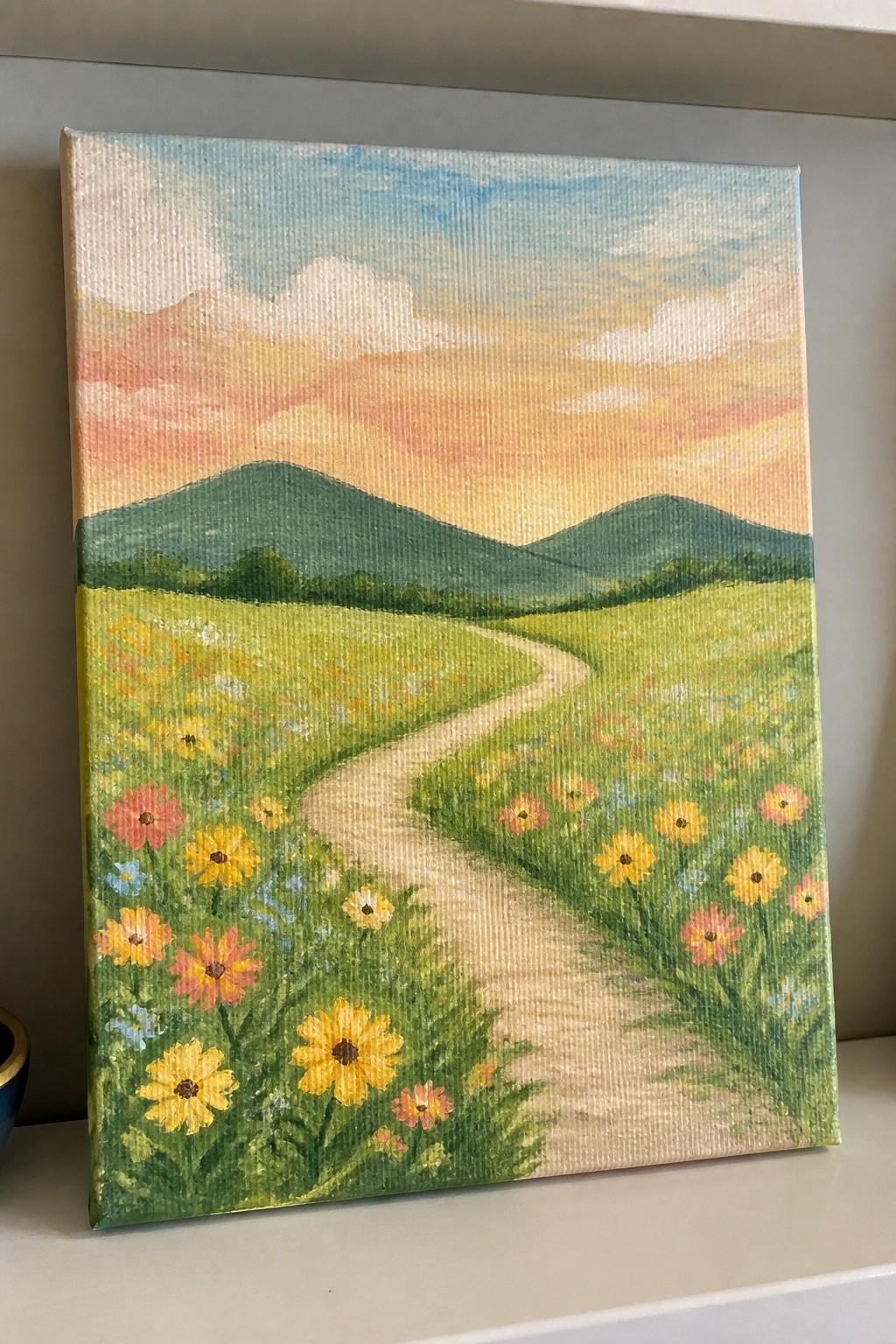Winding path through vibrant wildflower meadow under colorful sunset sky with green hills