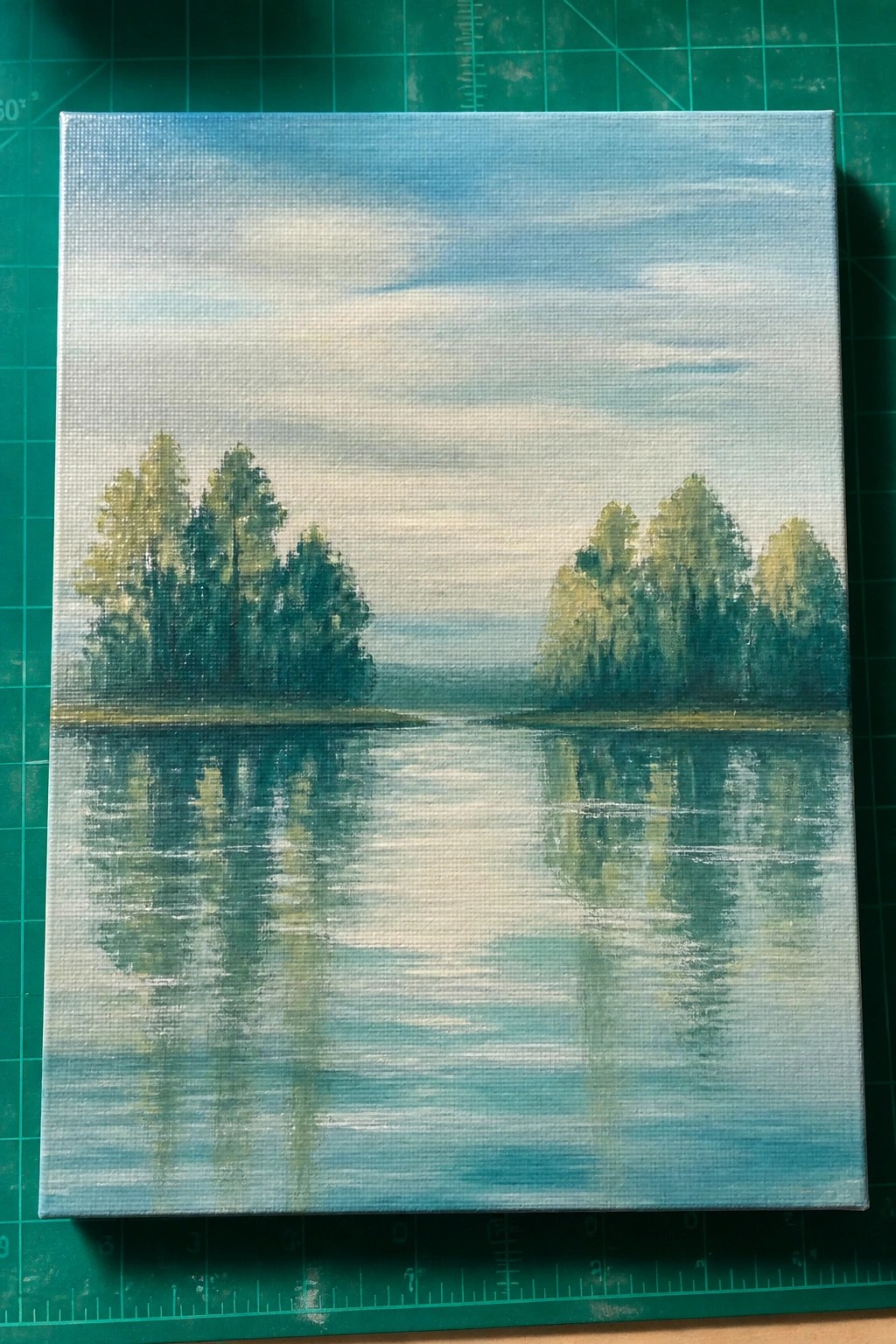 Painting of calm lake with tree reflections under cloudy blue sky on canvas.