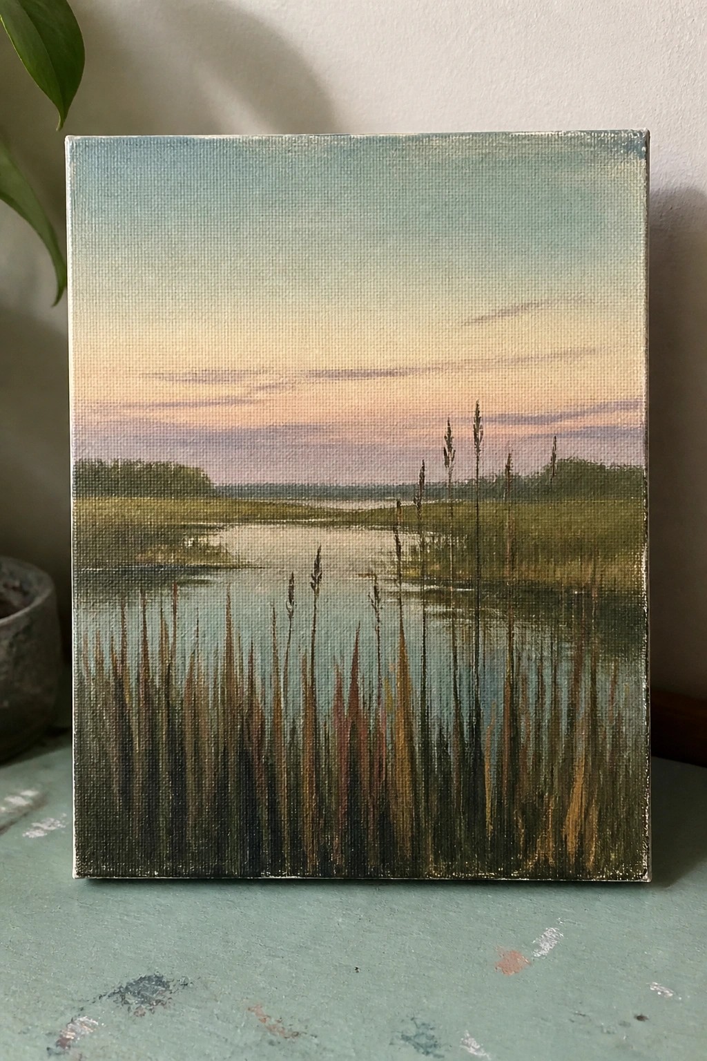 Painting of marsh at sunset with tall grasses reflecting in calm water under pastel sky.