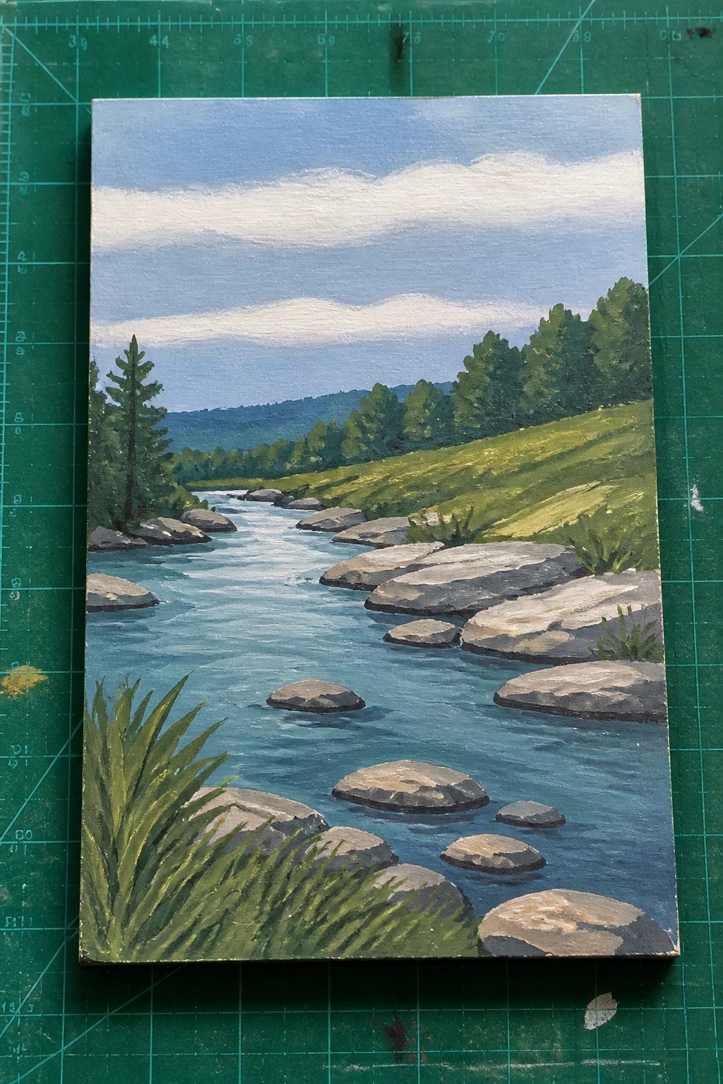 Painted river landscape with blue water, gray rocks, green trees and distant hills.