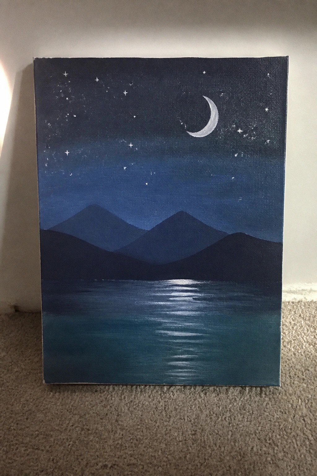 Acrylic painting of a crescent moon and stars above dark mountains with a reflection in a blue lake at night.
