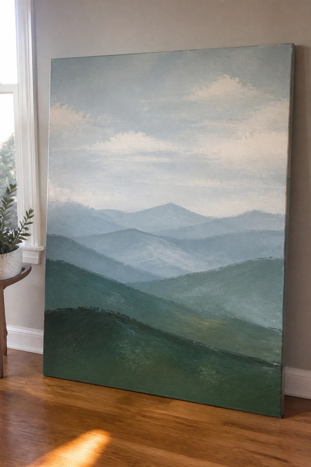 Large painting of misty layered blue mountains over rolling green hills against wall