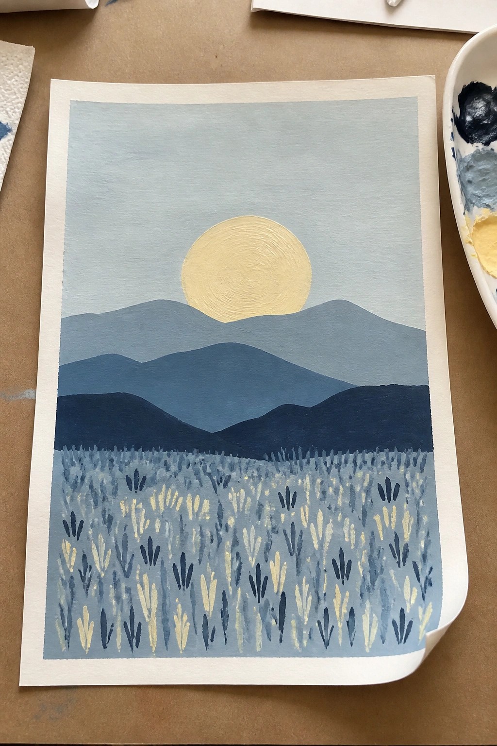Watercolor landscape of yellow sun above layered blue mountains and floral field