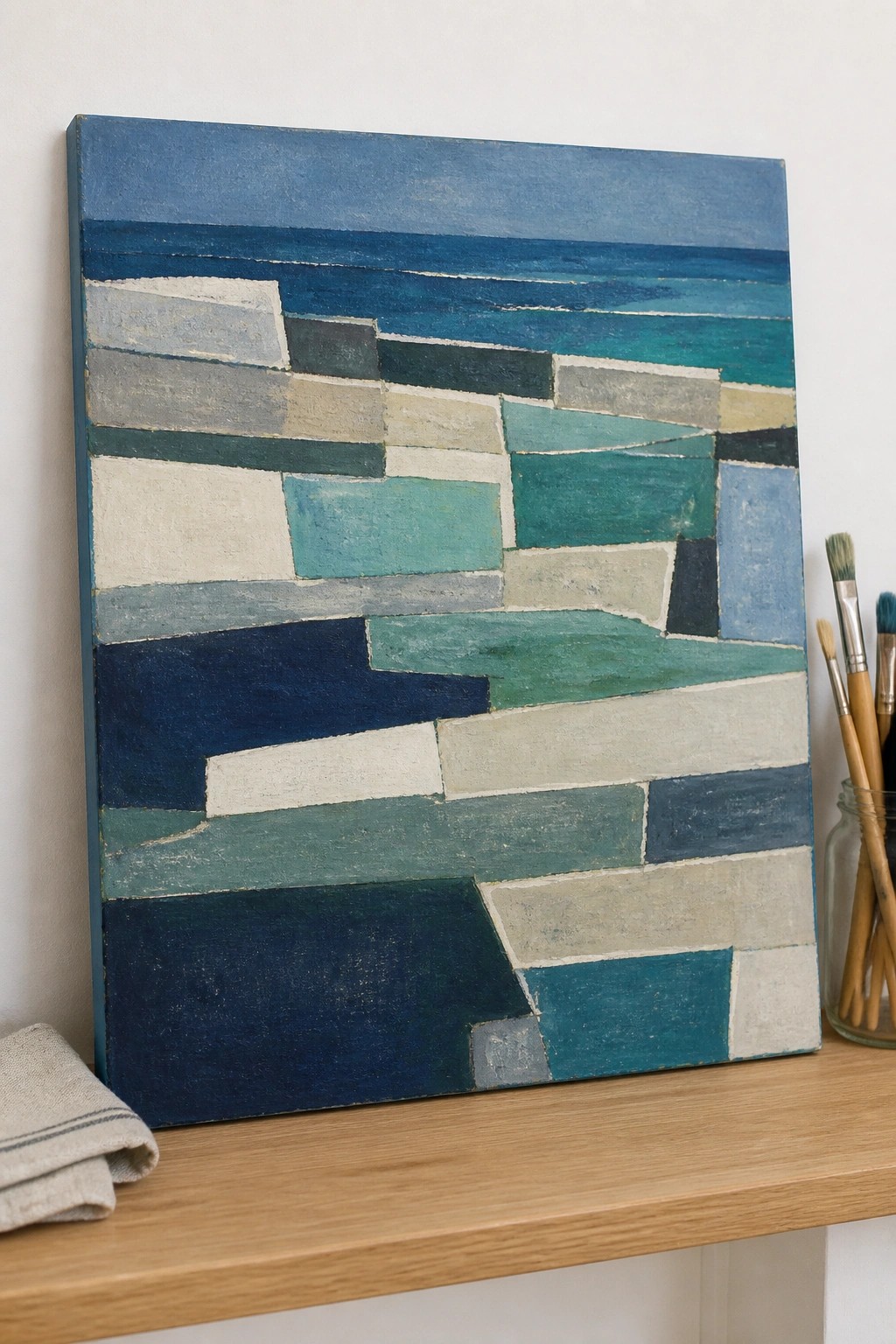 Abstract geometric painting in blues and greens on wooden shelf with brushes and cloth