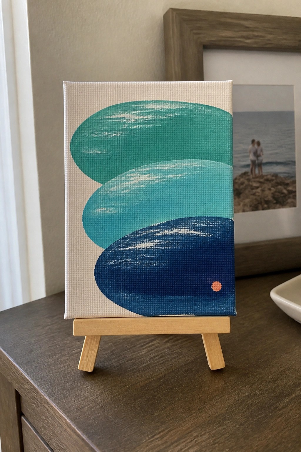 Abstract painting with three overlapping teal-blue ovals and orange dot on wooden easel