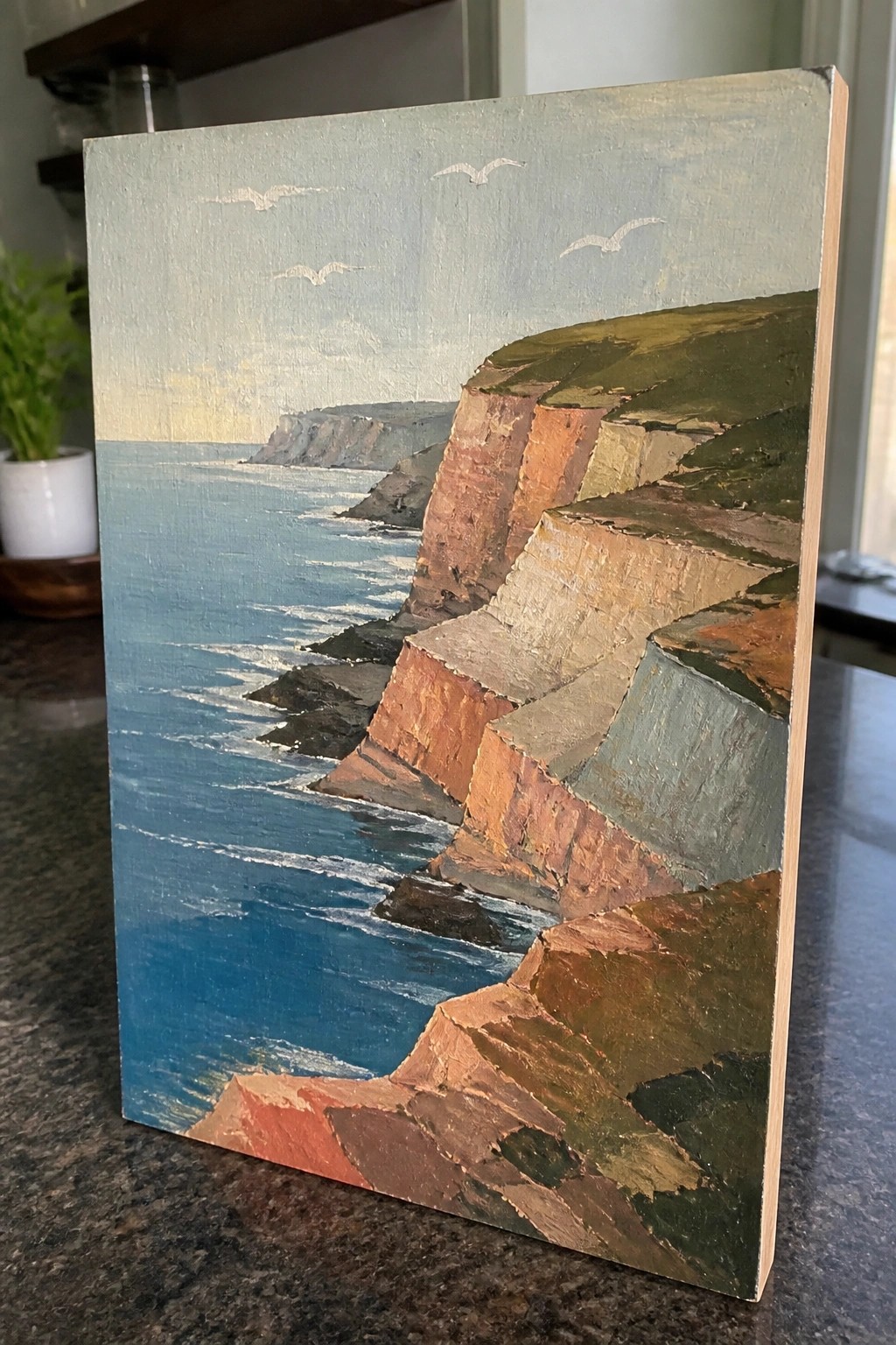 Layered coastal cliffs in warm tones overlook blue ocean waves with flying seagulls.