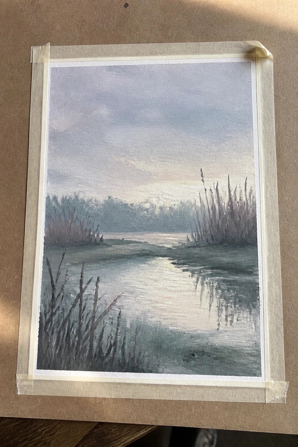 Serene landscape painting of calm river with reflective light, reeds, and cloudy sky, taped down.