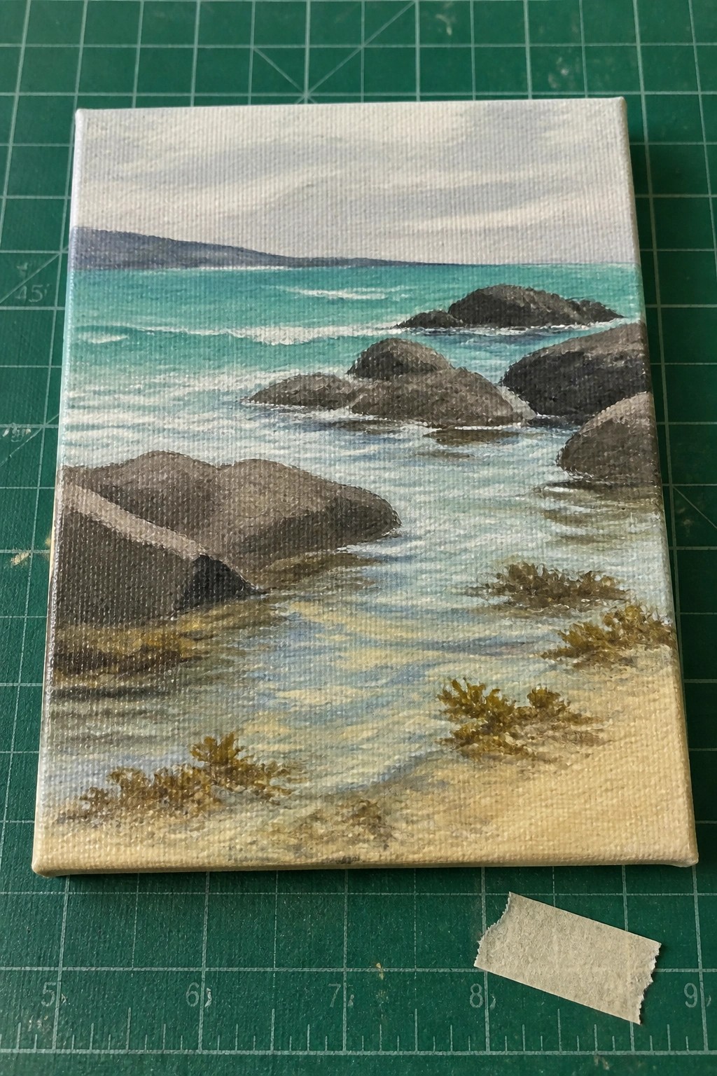 Canvas painting of turquoise sea, waves, dark rocks and sandy shore with shrubs