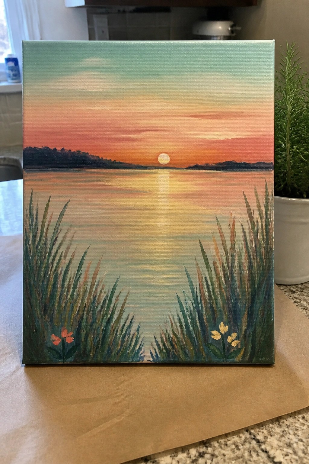 Sunset painting on canvas with orange sky, sun reflection, silhouetted hills, and foreground reeds.
