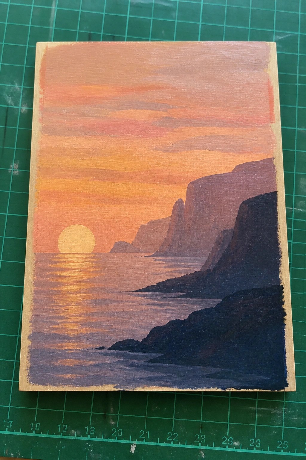 Painting of sunset over ocean with pink-orange sky, glowing sun, and dark cliffs