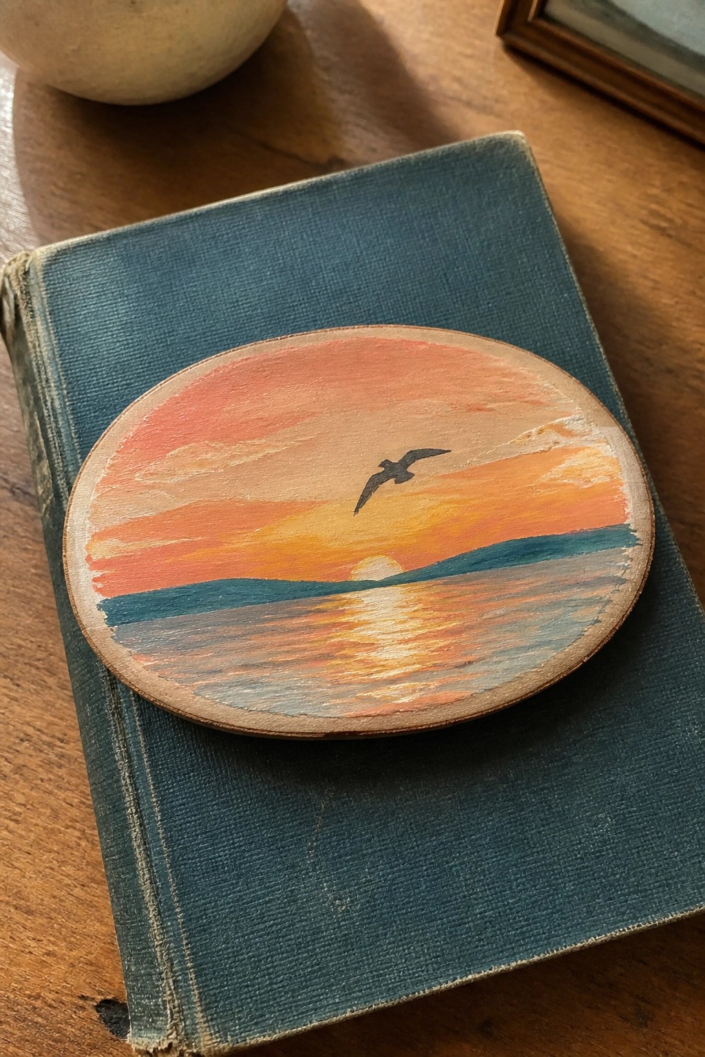 Worn blue book with oval sunset painting of bird flying over reflective water.
