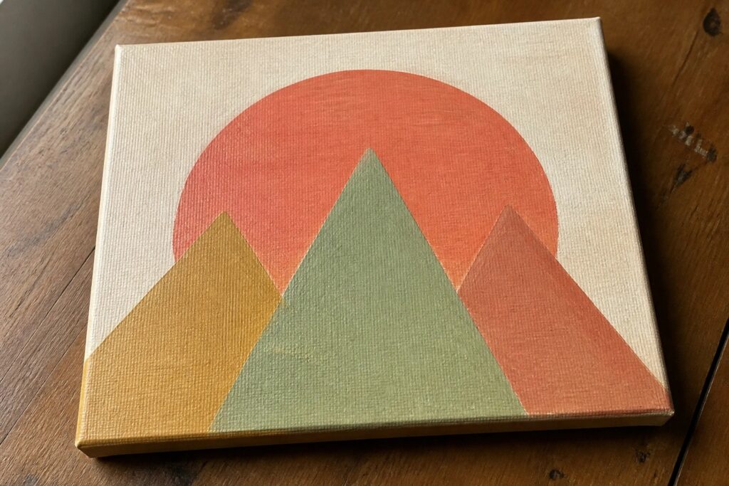 Abstract painting of red sun above green and yellow mountain triangles on canvas
