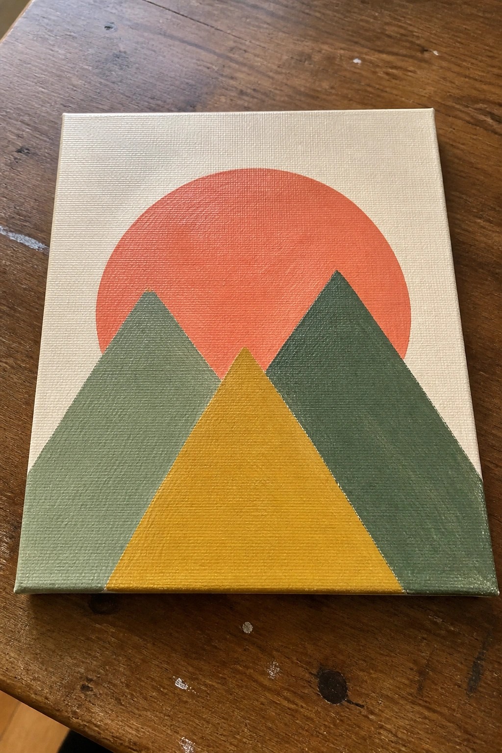 Abstract painting of red sun above green and yellow mountain triangles on canvas