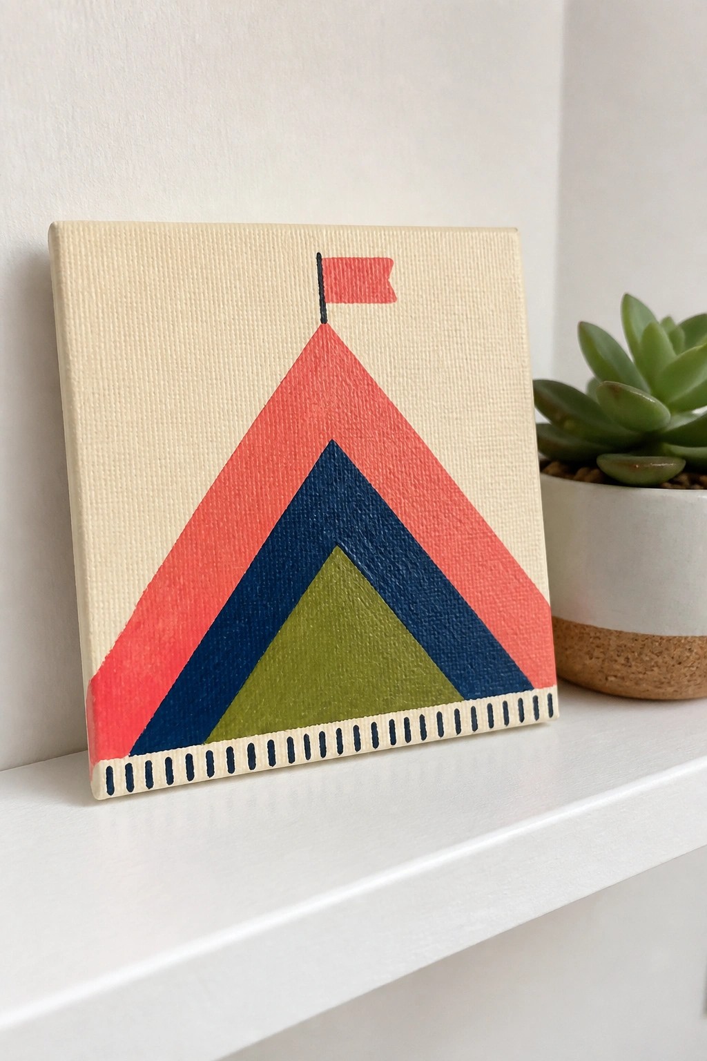 Colorful layered triangle painting on canvas with red flag beside succulent plant on shelf.