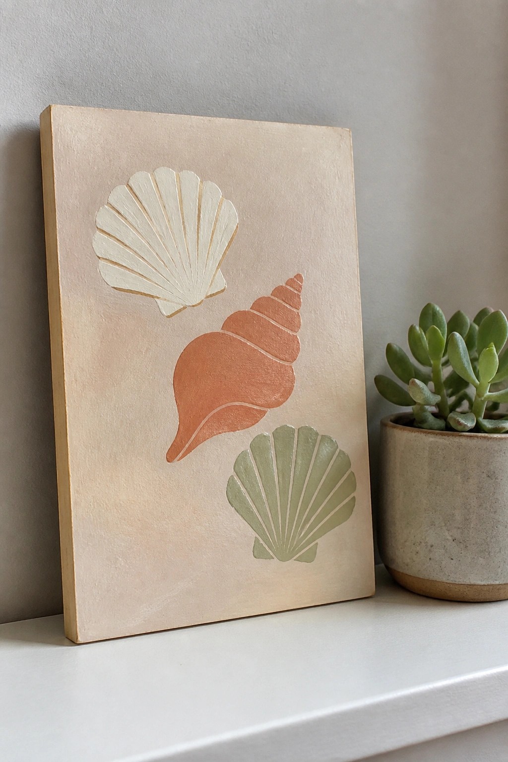 Beige wooden panel with cream, coral, and sage seashell prints beside a succulent.