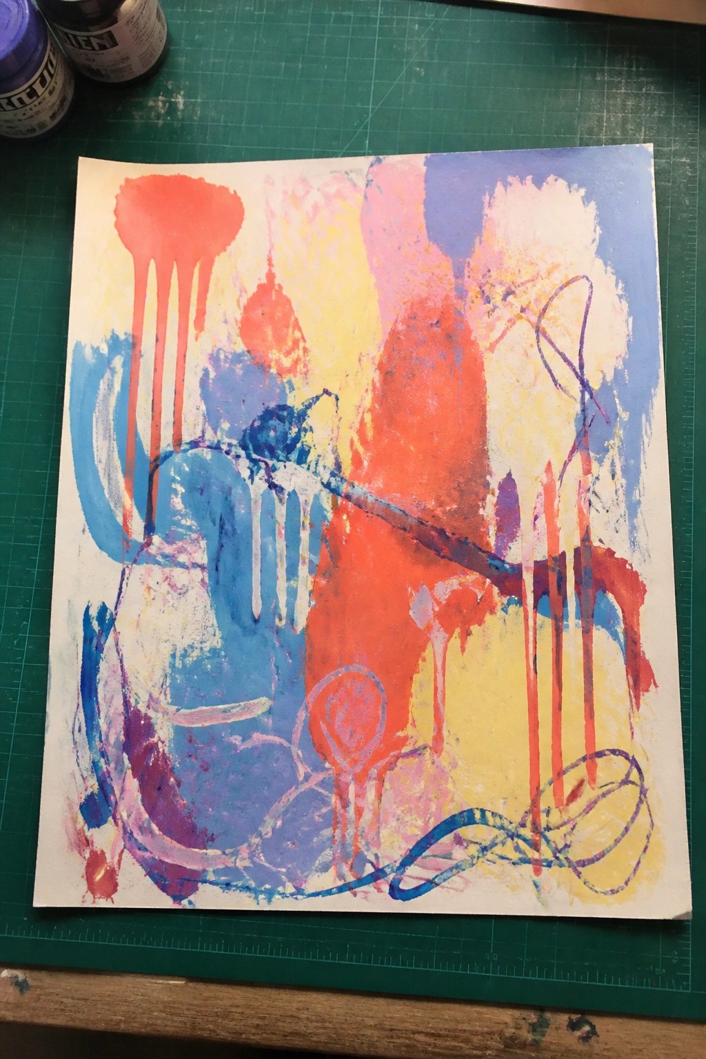 Abstract painting with red blue yellow drips and strokes on white paper over green mat