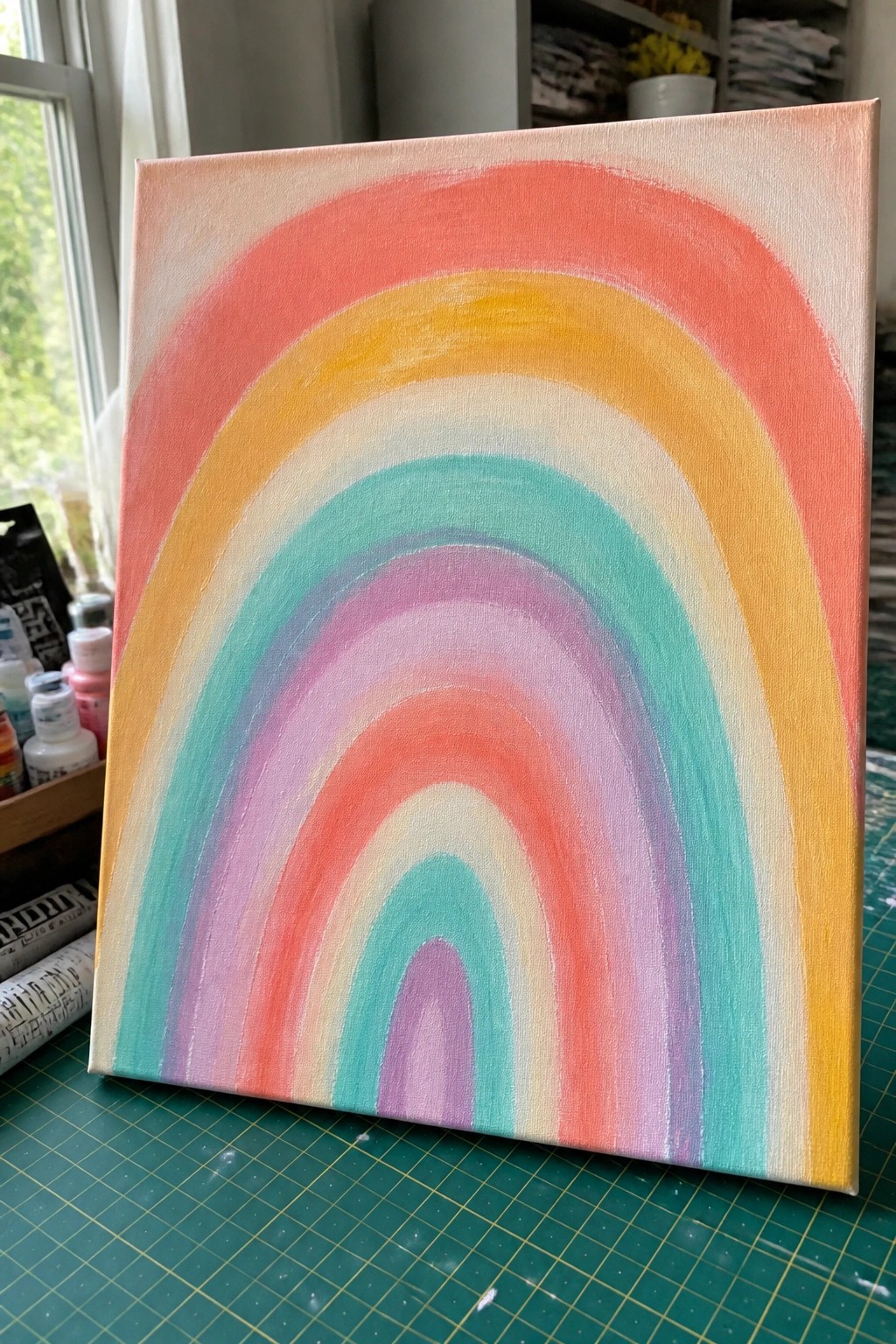 Colorful rainbow painting on canvas resting on green cutting mat amid art supplies