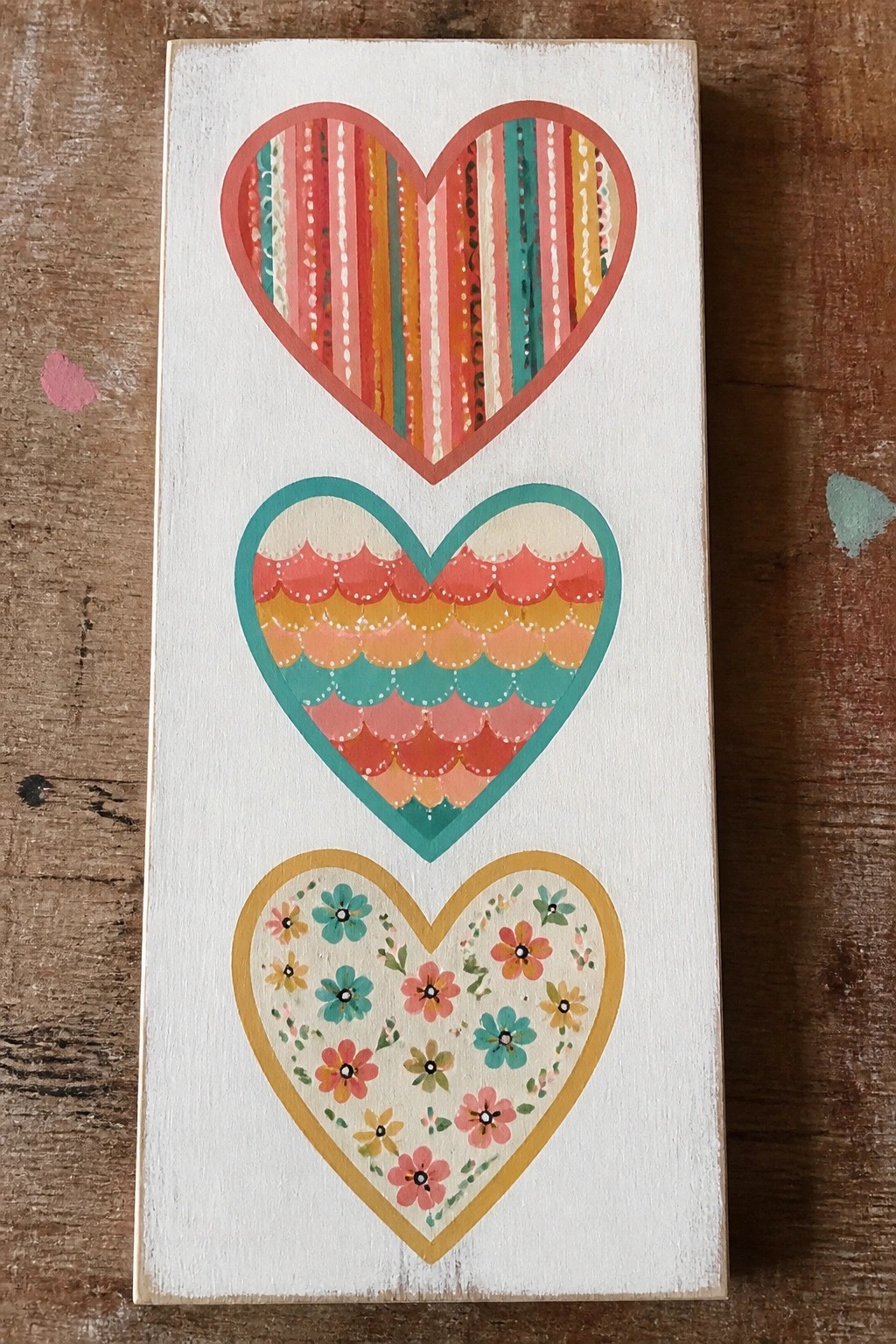 Three stacked hearts on white wood: striped, scalloped, and floral patterns.
