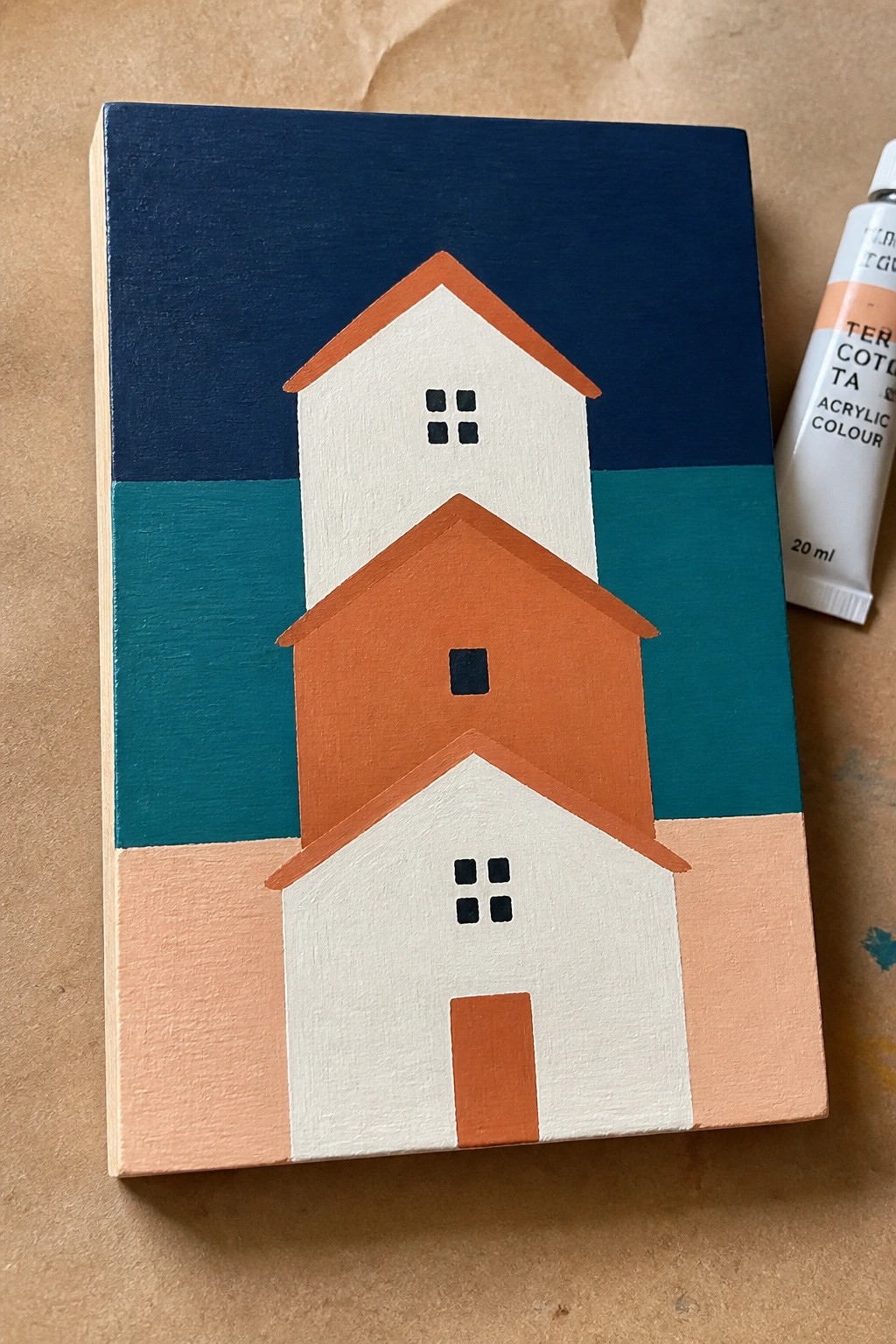 Three stacked geometric houses in white and orange with paint tube beside it.