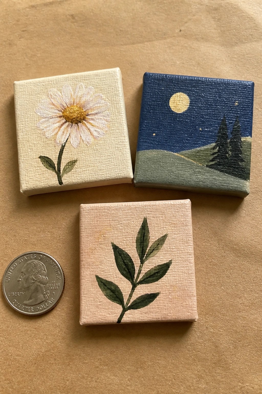 Three miniature paintings of daisy, night landscape, and leaves beside a quarter coin.