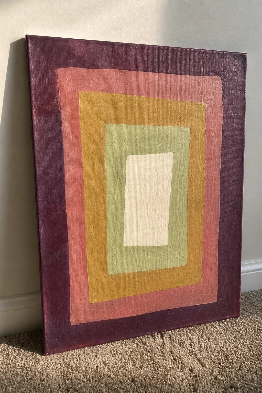 Abstract painting with concentric rectangles in purple, pink, yellow, green, and cream leaning on carpet