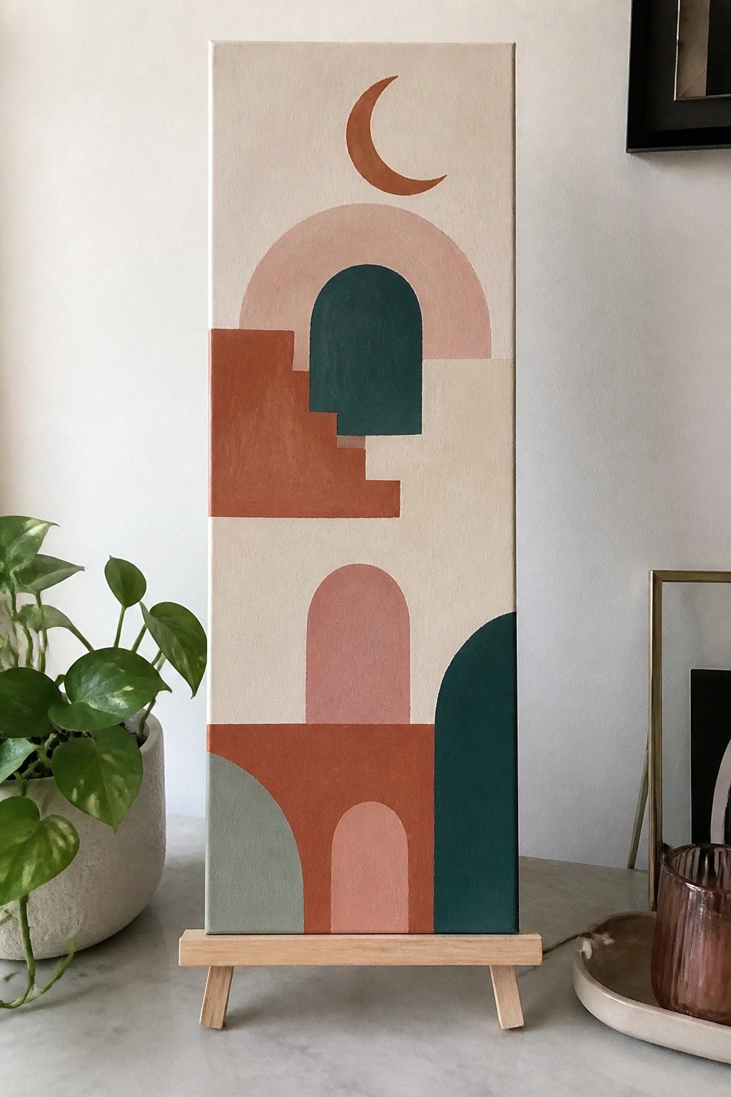 Abstract artwork with arches, crescent moon, steps, and earthy tones on wooden stand.