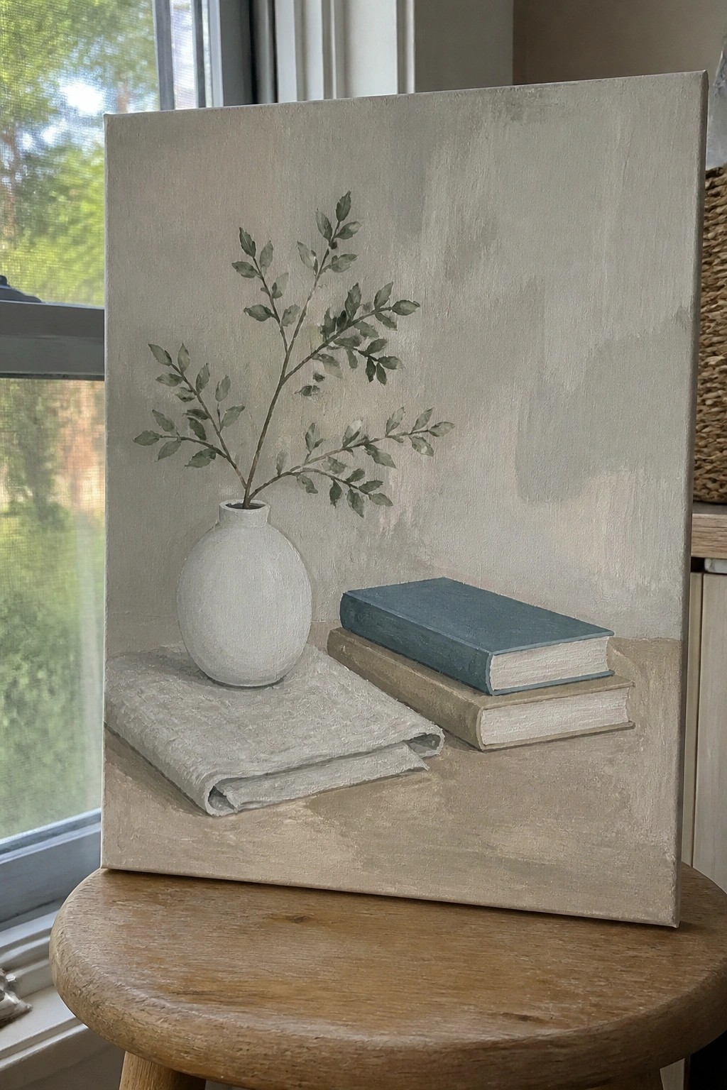 Minimalist still life painting of white vase with green leaves beside stacked books on cloth