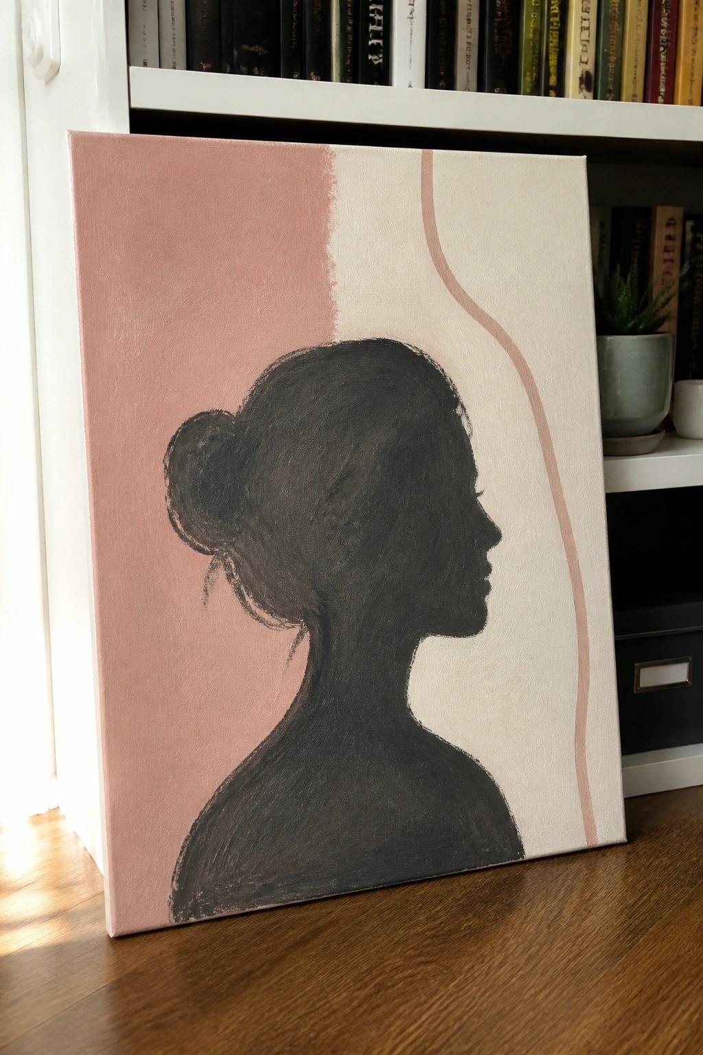 Canvas painting of woman's black silhouette with bun on pink-beige background