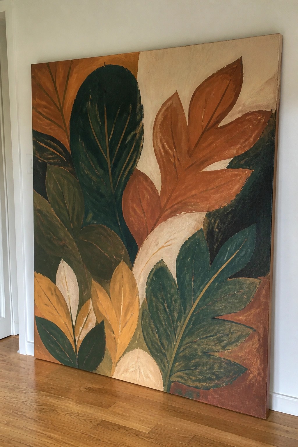 Large abstract painting of overlapping leaves in green, brown, and orange tones leaning on floor