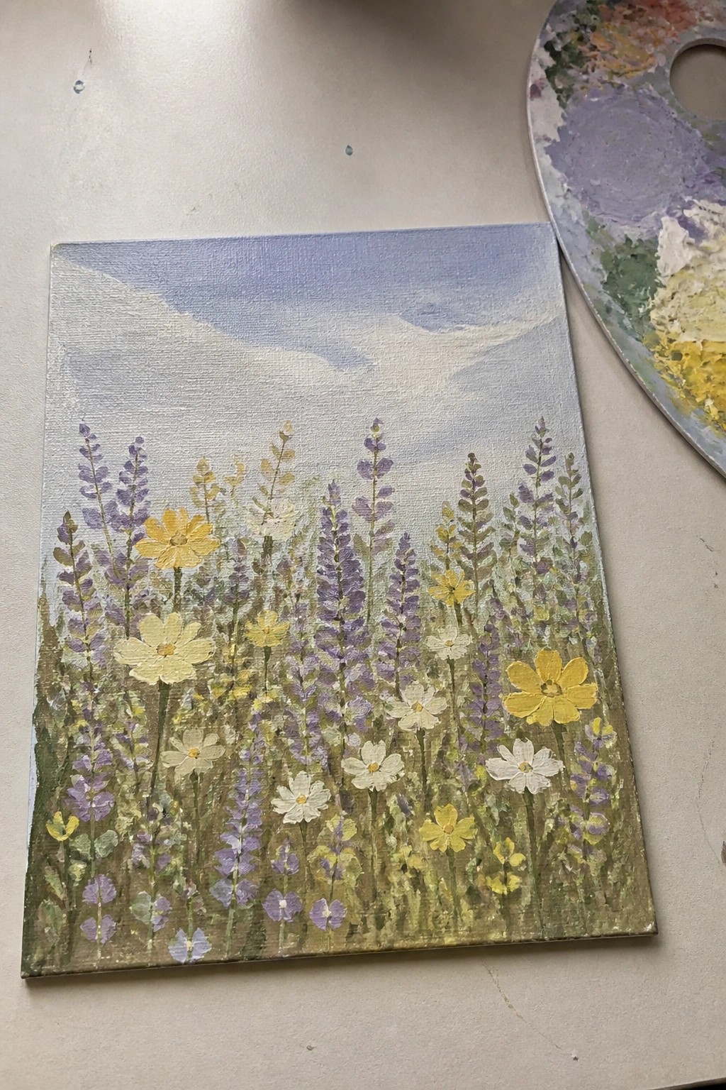 Canvas painting of wildflowers in purple, yellow, and white with palette nearby