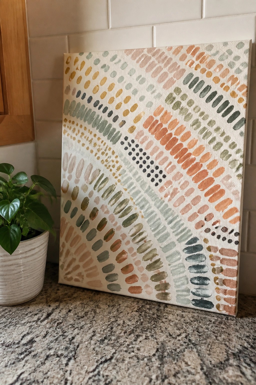Abstract canvas with colorful dots and strokes beside potted plant on granite counter
