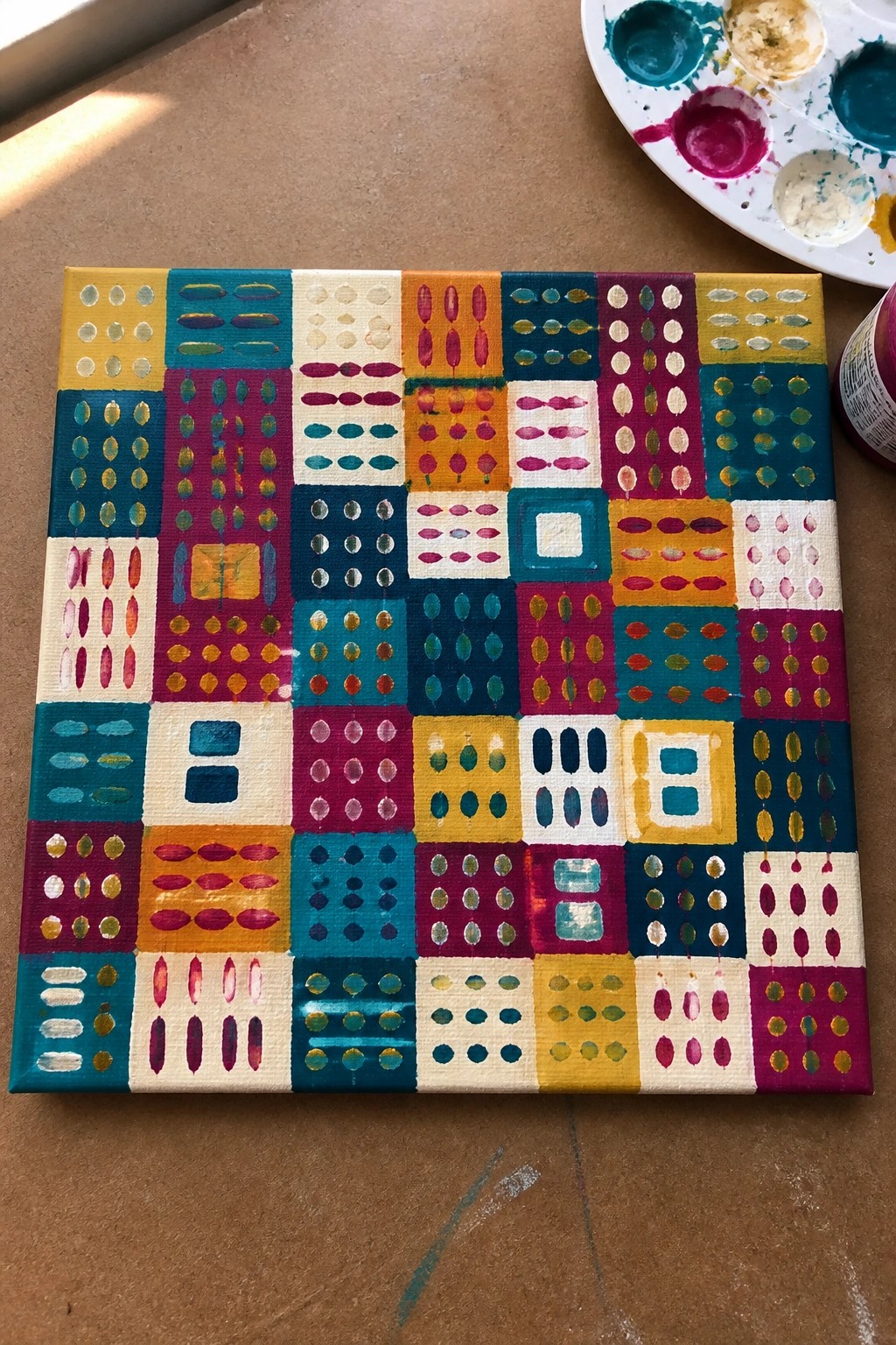 Colorful abstract grid painting on canvas beside paint palette and supplies.