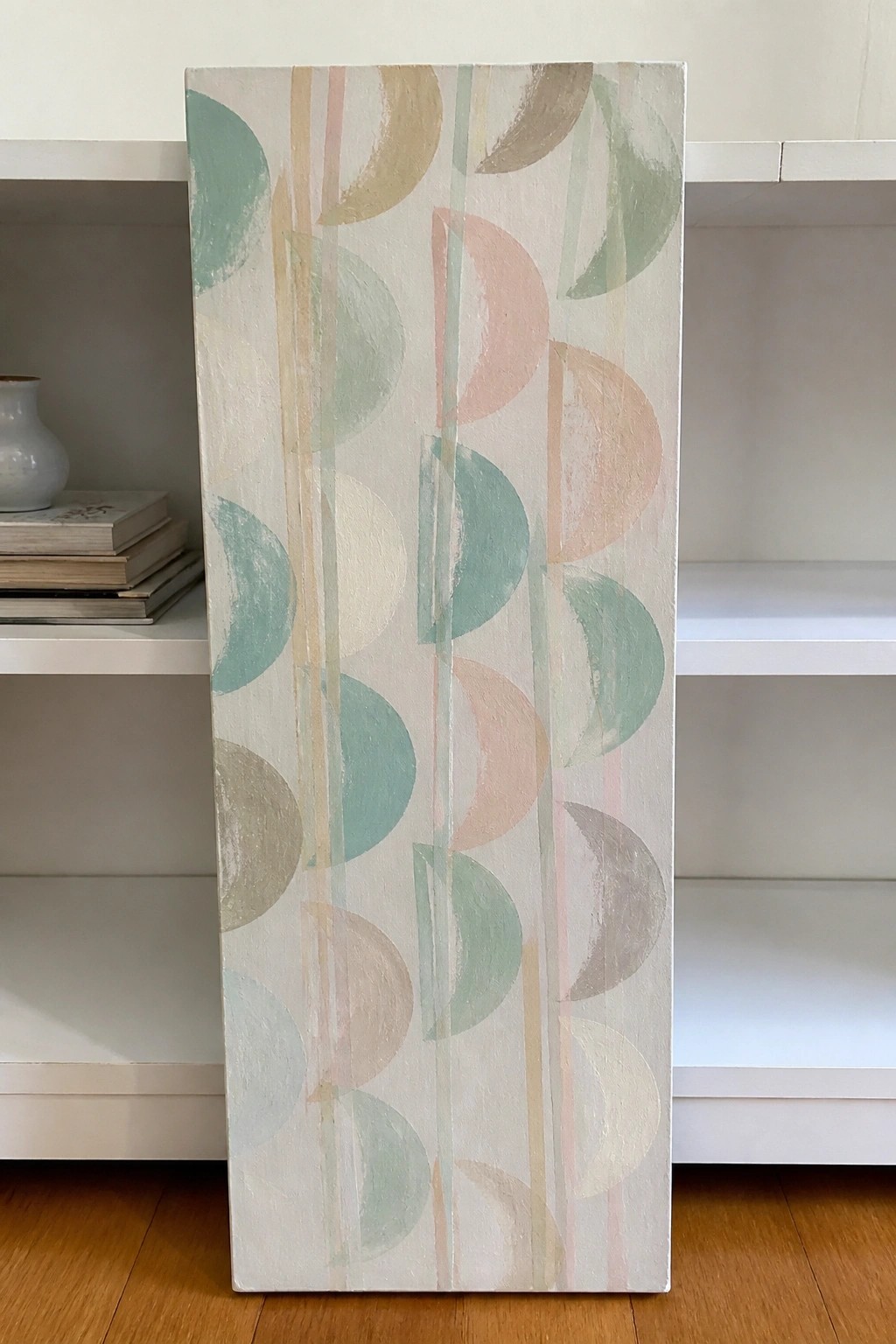 Vertical abstract canvas with pastel semicircles and stripes leaning on white shelves