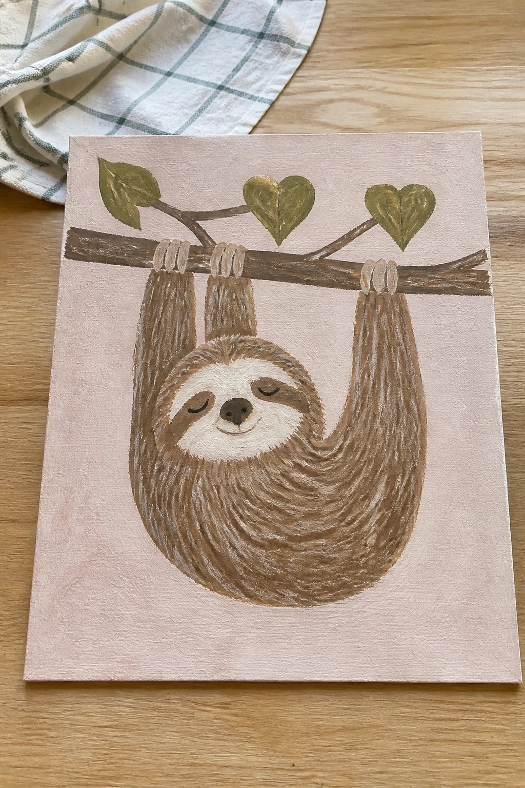 Cute cartoon sloth hanging from branch with green heart leaves on pink canvas