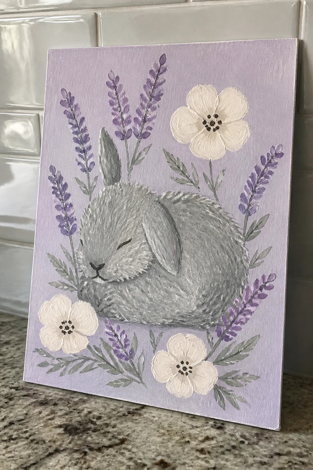 Sleeping gray bunny amid white flowers and lavender sprigs on light purple canvas