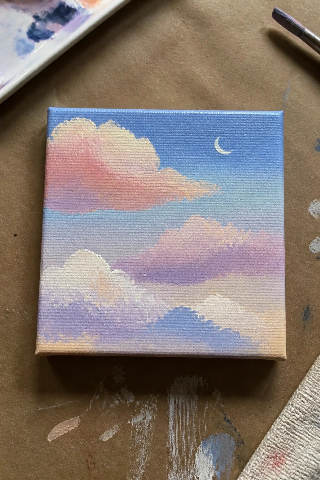 Miniature canvas painting of layered pastel clouds in blue sky with crescent moon